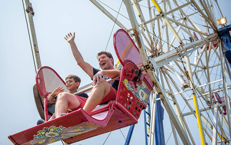 Fairgoers ride the ferris wheel, and wave to family down below.