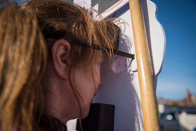 Carla Cooper peers out the cut out eyes of her Trump head sign.
